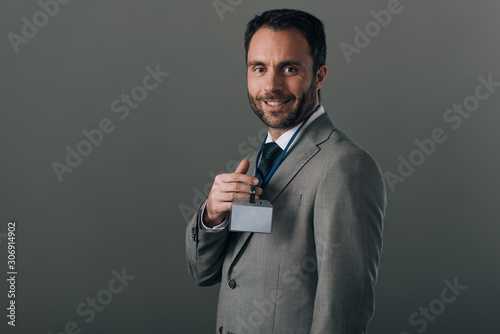 Smiling man in suit holding badge with copy space isolated on grey