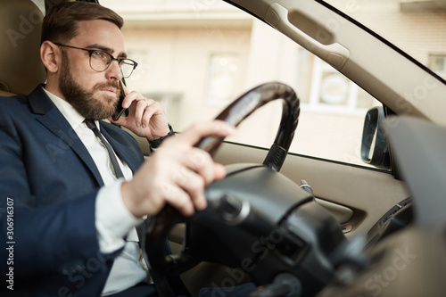 Young serious businessman in eyeglasses talking on mobile phone and driving the car © AnnaStills