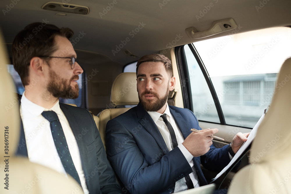 Young bearded businessman holding document and talking to his partner during driving in the car Young bearded businessman holding document and talking to his partner during driving in the car