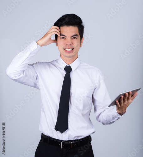 Portrait handsome young asian man wearing a white shirt holding smart phone or tablet stressed and anxiety isolated on gray background in studio. Asian man people. business success concept.