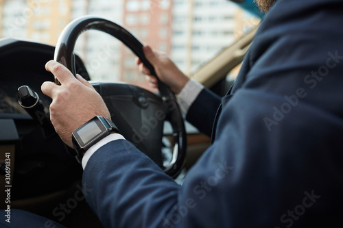 Close-up of man in suit holding wheel and driving his car in the city