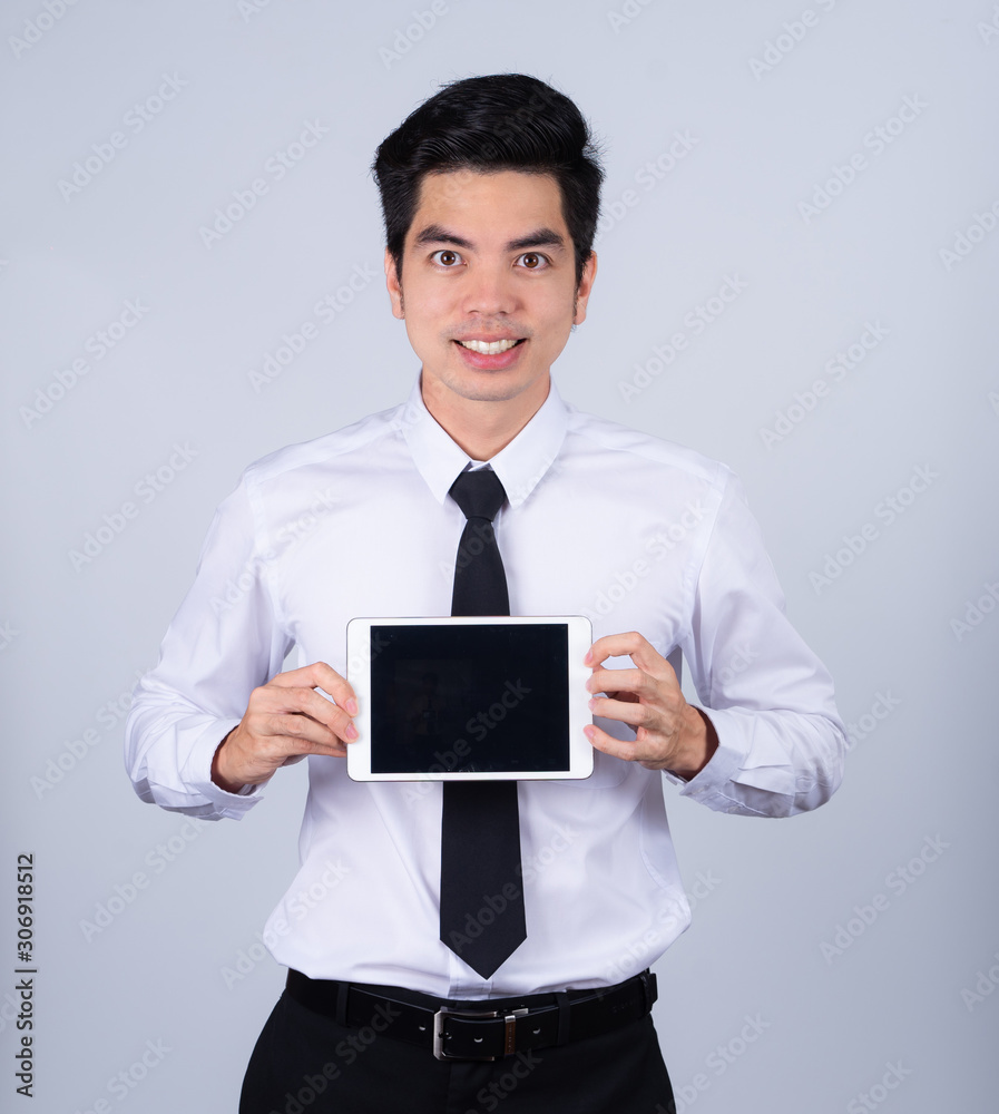 Portrait handsome young asian man wearing a white shirt holding smart phone or tablet smile and happy isolated on gray background in studio. Asian man people. business success concept.