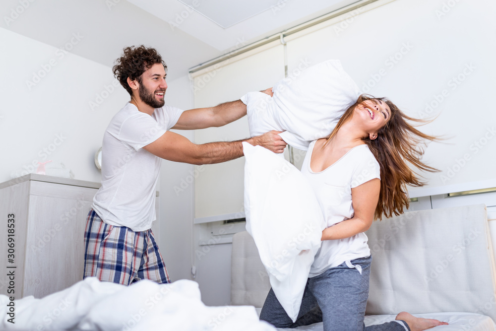 Couple having a fun while pillow fight. Young happy couple beat the pillows on the bed in a bedroom at home. Couple having a fun while pillow fight. Young happy couple beat the pillows on the bed in a bedroom at home.