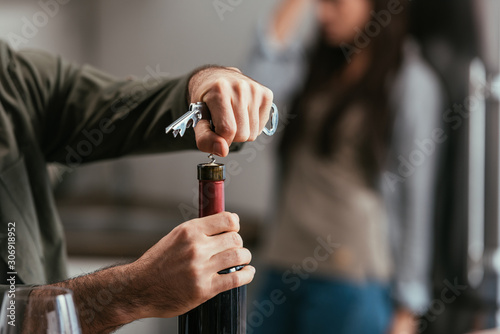 Selective focus of man opening wine bottle and worried wife at background