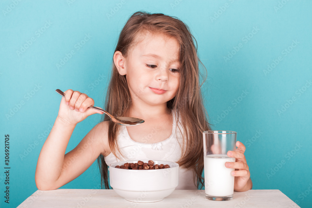 Cute little girl eating chocolate cereal with milk for breakfast