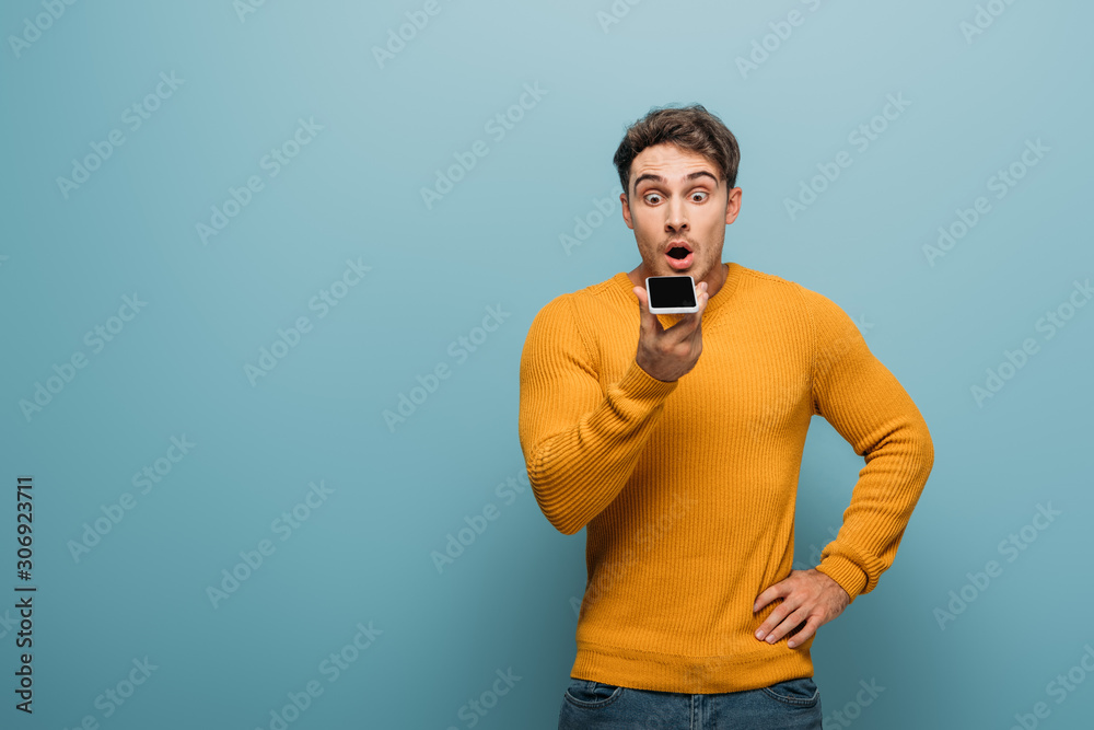 shocked handsome man using smartphone, isolated on blue shocked handsome man using smartphone, isolated on blue