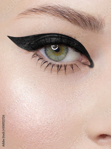 Glamour close-up portrait of beautiful woman model face with winged black eyeliner make-up, clean skin on white background. Long eyelashes and thick eyebrows.