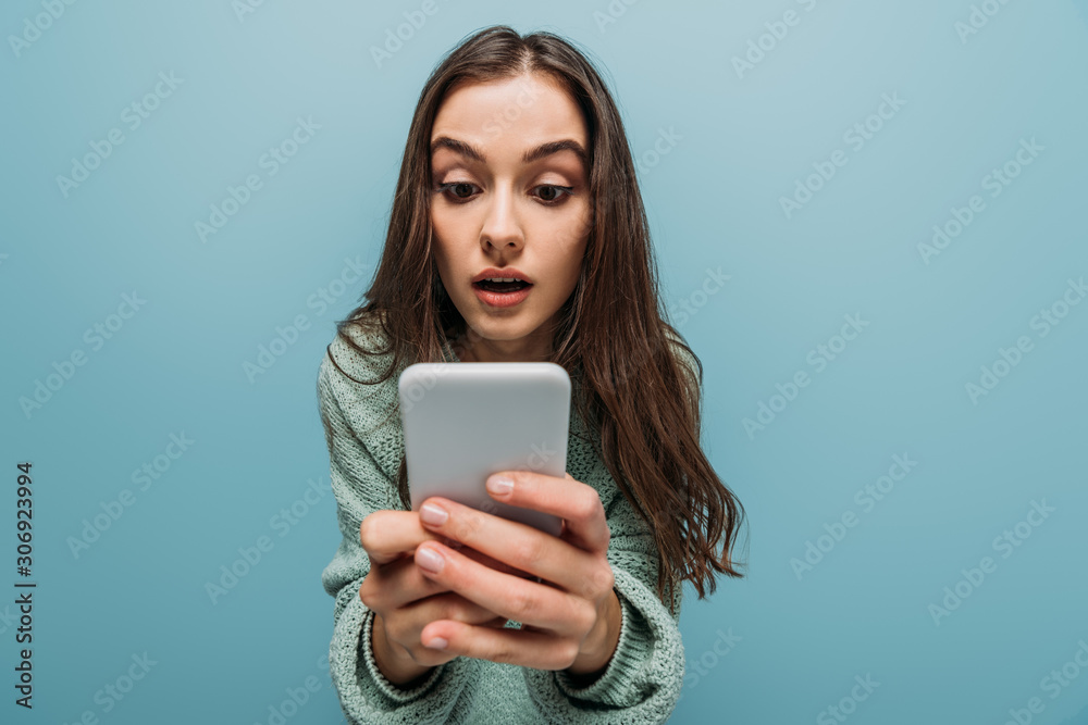surprised girl using smartphone, isolated on blue