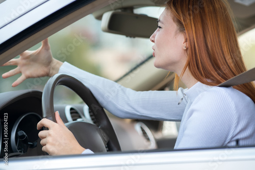 Closeup portrait of pissed off displeased angry aggressive woman driving a car shouting at someone with hand fist up. Negative human expression consept. © bilanol
