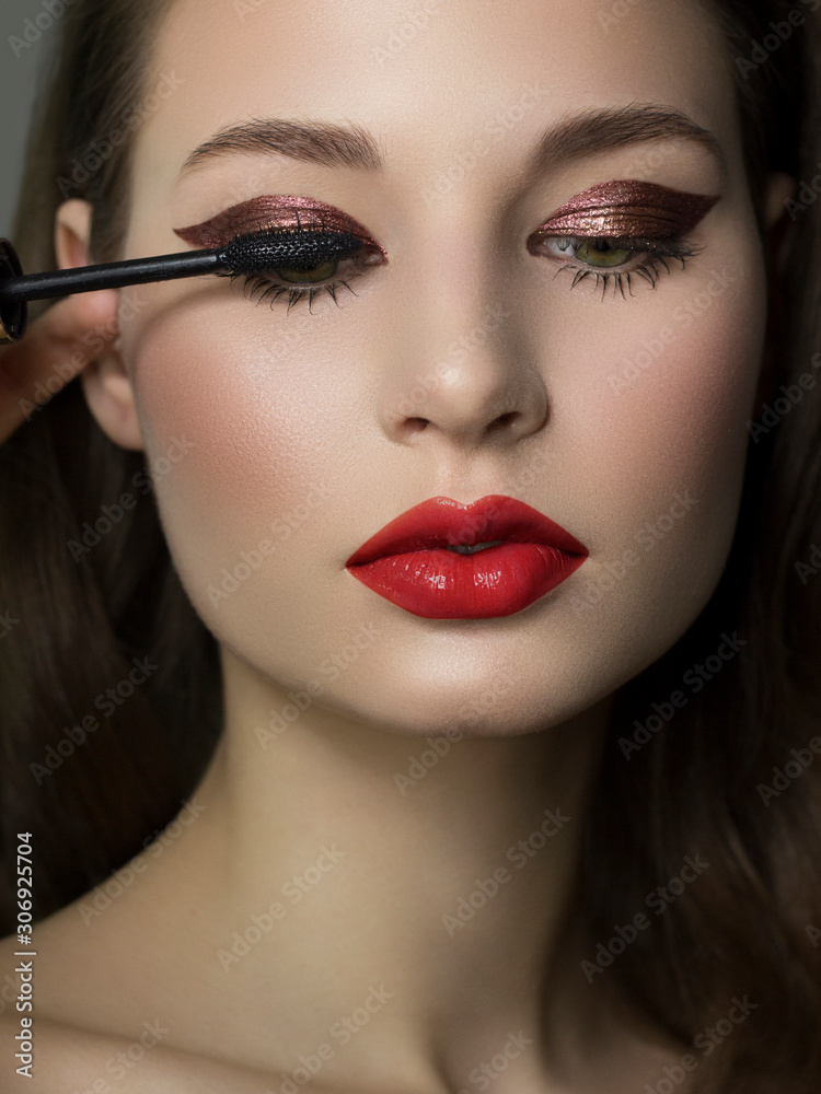 Close-up of female green eye with burgundy thick eyeliner. Mascara brush colors extra long eyelashes. Thick beautiful eyebrows and red lips. Clean smooth skin. Cosmetology and spa