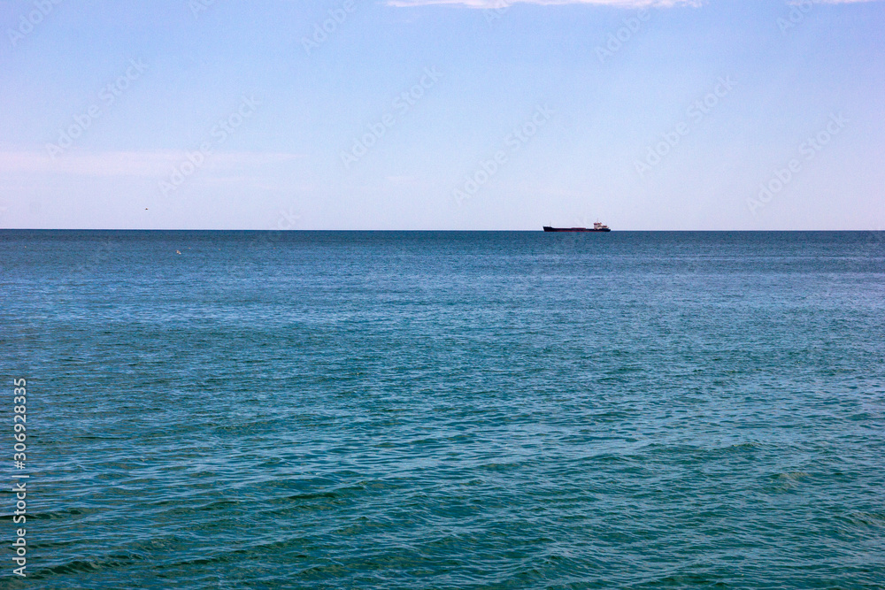 Beautiful summer seascape. Blue water surface and a ship on the horizon.