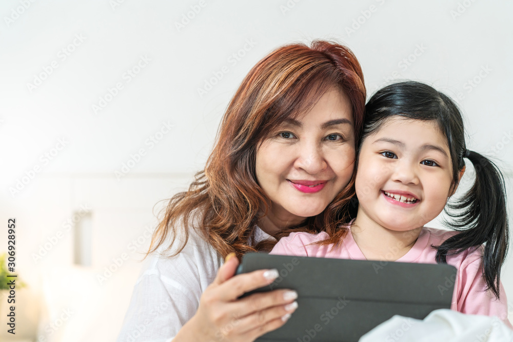 Portrait of two generations of women looking camera. Cute little girl hug granny enjoy time at home, smiling, using tablet computer at home. Happy lifestyle concept. Portrait of two generations of women looking camera. Cute little girl hug granny enjoy time at home, smiling, using tablet computer at home. Happy lifestyle concept.