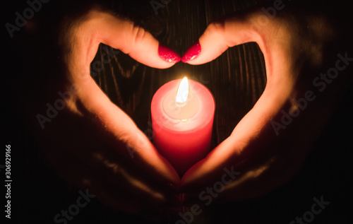 Heart-shaped female hands around  burning red candle