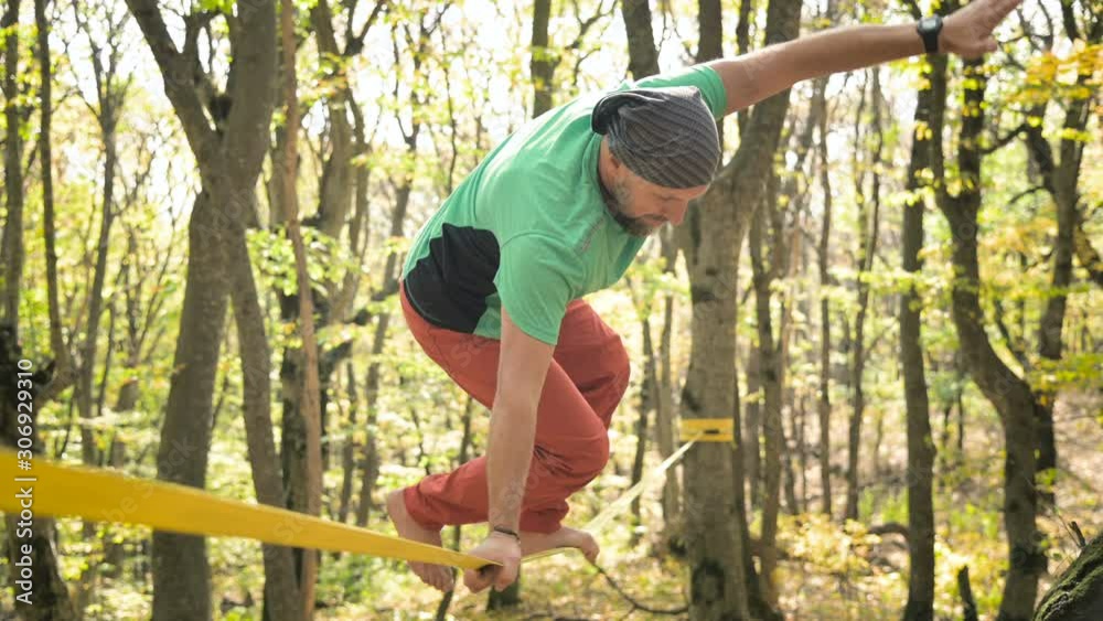 An aged man is trying to stand on a slackline sling to practice balance. The concept of physical development in adulthood An aged man is trying to stand on a slackline sling to practice balance. The concept of physical development in adulthood