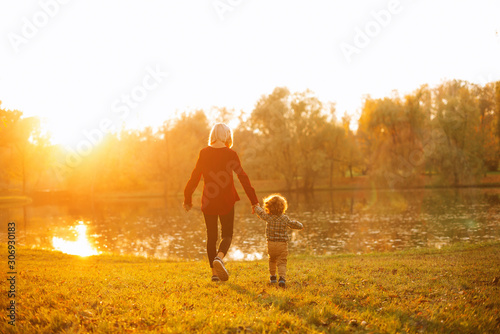 A young mother is walking with her son near a lake.