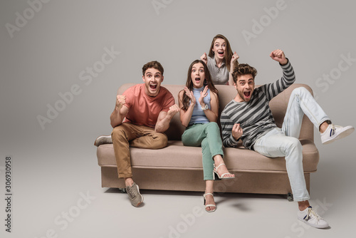 Φωτογραφία happy young friends cheering and sitting on sofa on grey