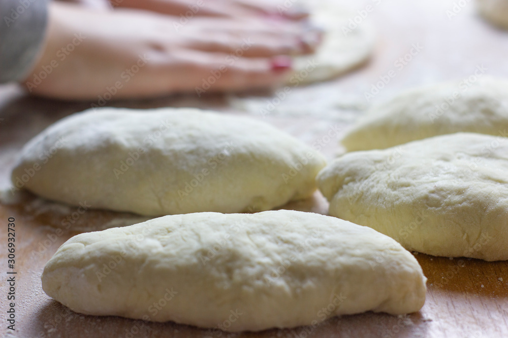 Raw pies for baking in the oven on the background of the female hands of the chef who makes it all.