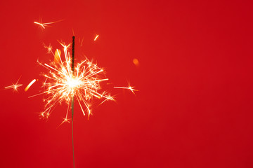 Close up of Brightly burning sparkler on a red background with lots of sparks.