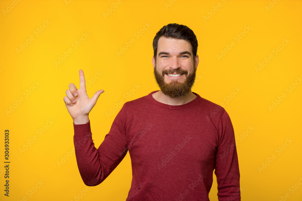 Smiling barded man in red sweater is showing up to a copy space on yellow background. Smiling barded man in red sweater is showing up to a copy space on yellow background.