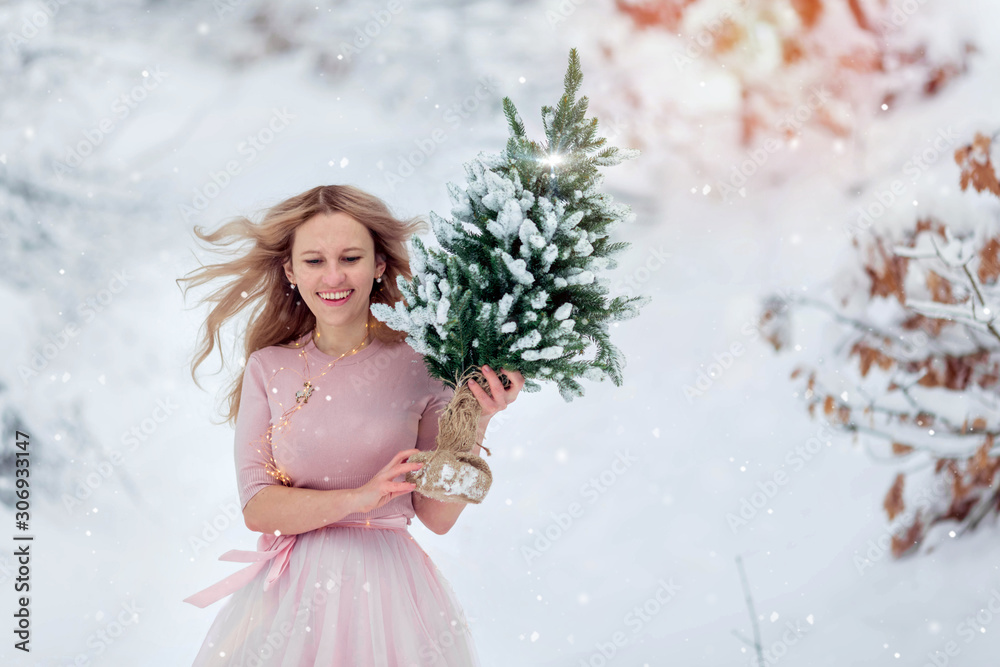 Happy woman holding a green Christmas tree on the background of snow.