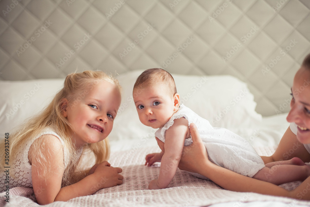 Young beautiful mother holds a baby. Little sister kisses her little sister. Baby. Children bedroom. Young beautiful mother holds a baby. Little sister kisses her little sister. Baby. Children bedroom.