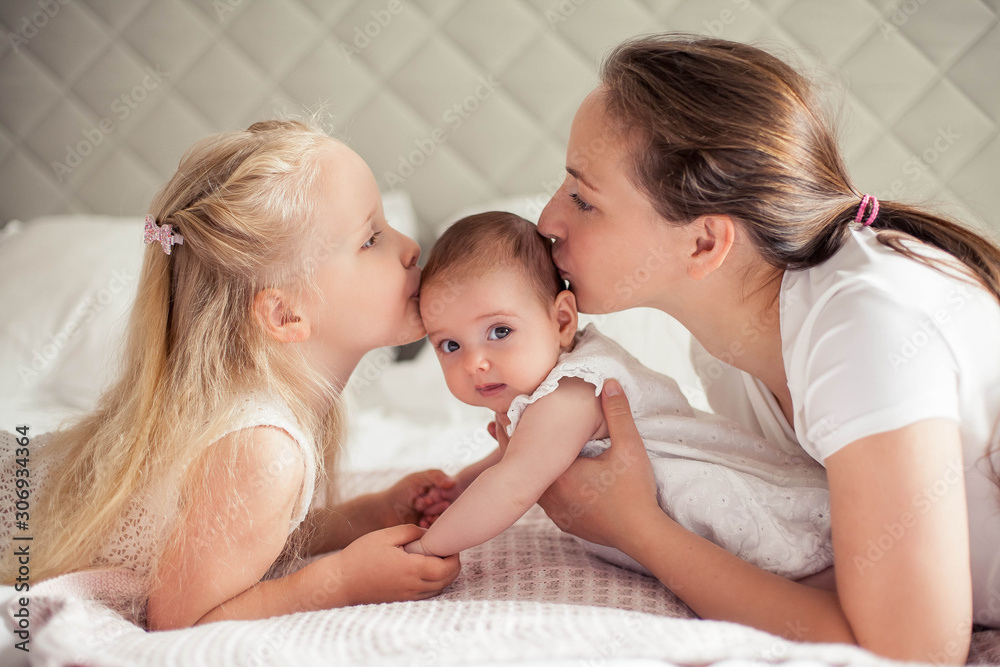 Young beautiful mother holds a baby. Little sister kisses her little sister. Baby. Children bedroom.