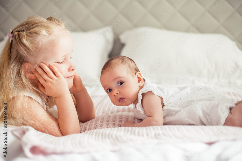 Young beautiful mother holds a baby. Little sister kisses her little sister. Baby. Children bedroom. Young beautiful mother holds a baby. Little sister kisses her little sister. Baby. Children bedroom.