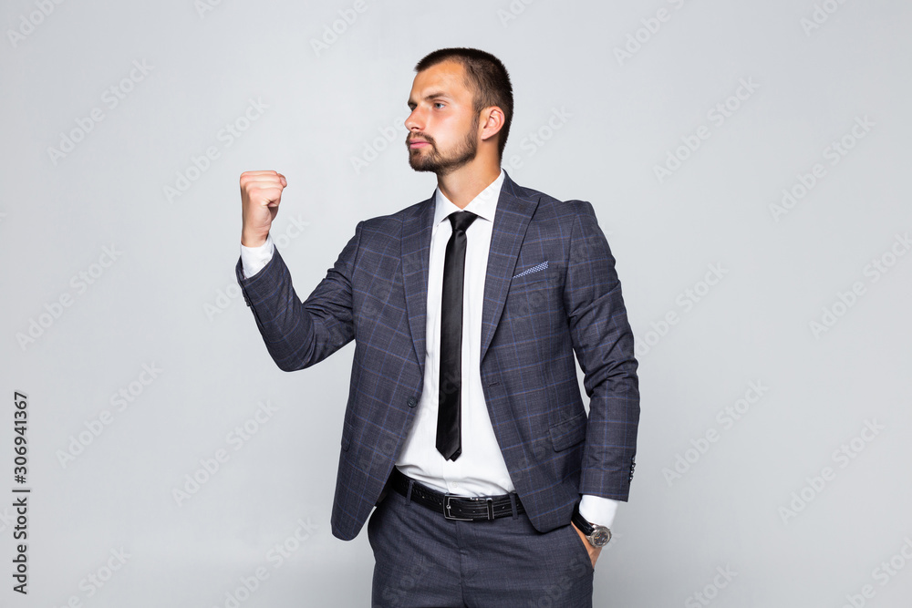 Young successful delighted businessman in formal suit screaming and clenching his fists isolated over gray background Young successful delighted businessman in formal suit screaming and clenching his fists isolated over gray background