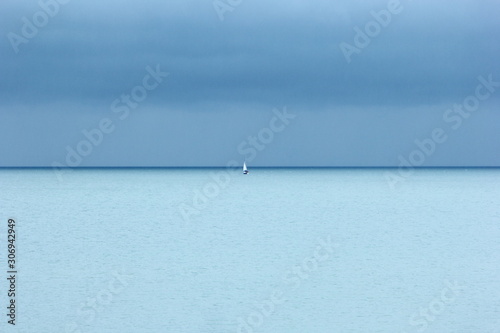 Small white yacht, turquoise blue sea and dark blue sky with clouds, a rainy day photo