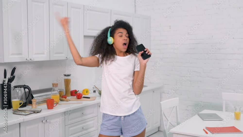 Young woman holding mobile like a microphone, singing and dancing. Having fun at the kitchen in the morning. Slowmotion. Young woman holding mobile like a microphone, singing and dancing. Having fun at the kitchen in the morning. Slowmotion.