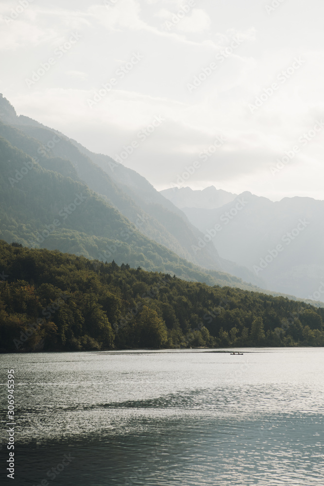Mountain lake Bohinj in Triglav National Park, Slovenia. Lake in the foreground, misty mountains in the background. Boat in the middle of lake. Sunrise on the lake