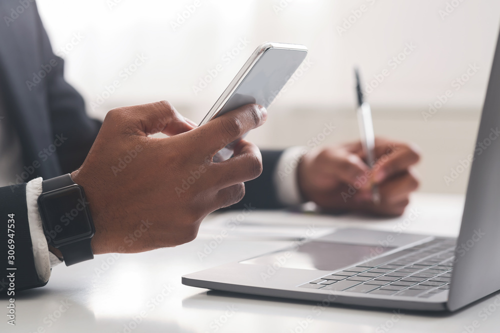 African american businessman using smartphone and taking notes in office African american businessman using smartphone and taking notes in office