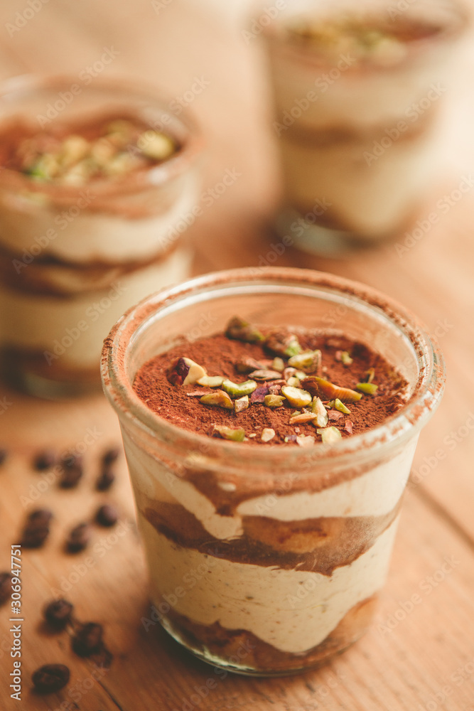 Tiramisu with pistachios and coffee in jars on a wooden countertop Tiramisu with pistachios and coffee in jars on a wooden countertop