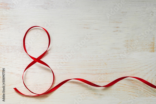 Red gift celebration ribbon waved in shape of number 8 (eight) on white wooden background. Greeting card with copy space for 8 March, International Women's Day