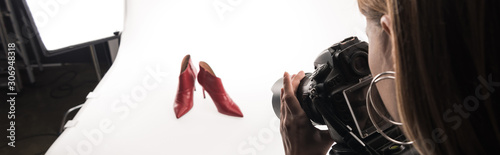 cropped view of commercial photographer making commercial photo shoot of female red heel shoes on white, panoramic shot