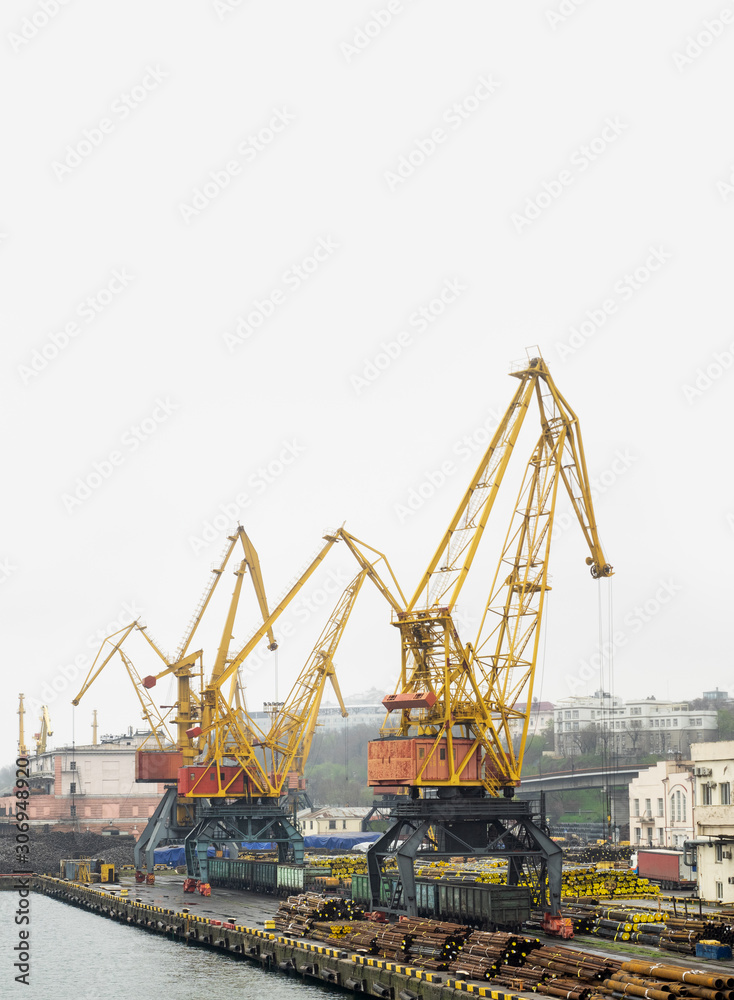Landscape of cargo terminal in Odessa port - portal cranes on a pier are loading of coal, pipes and metal, isolated on white. Freight transportation and export products of heavy industry from Ukraine.