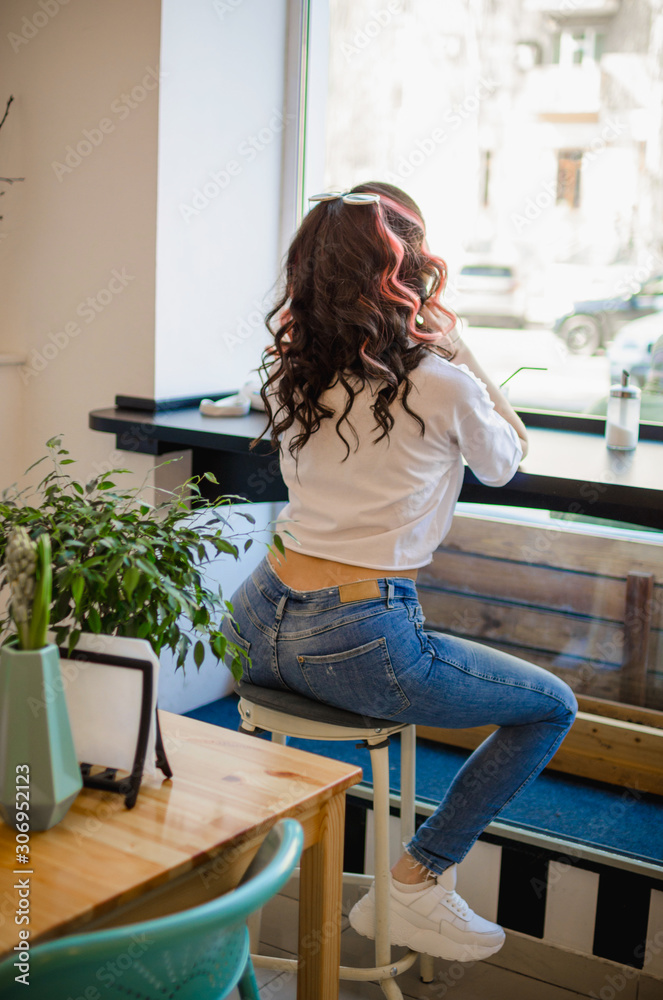 Stylish girl in a white T-shirt and jeans sits in a cafe on the bar stool.  Beautiful ass of a young, white girl in tight blue jeans. Bright closeup  photo. Stock Photo |