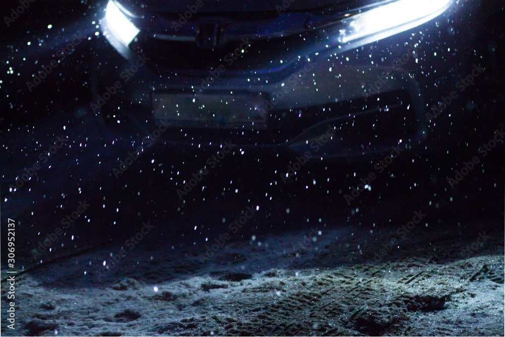 snowflakes during snowfall lit with light from car headlights at night on a road snowflakes during snowfall lit with light from car headlights at night on a road