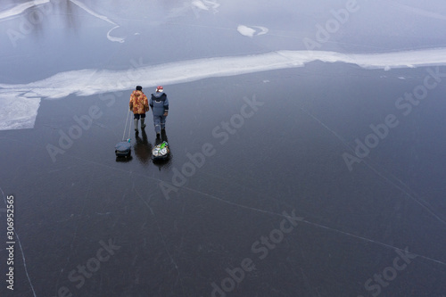 Icy surface of the river. Two fishermen return from fishing. They pull a sled with a catch. The view from the top.