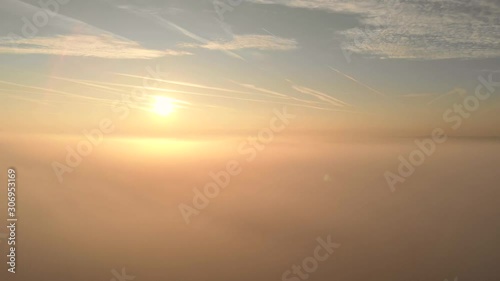 Drone flight above and through moving cloudscape with beautiful sun rays and blue sky covered by chemtrails during a sunrise. Ariplane point of view
