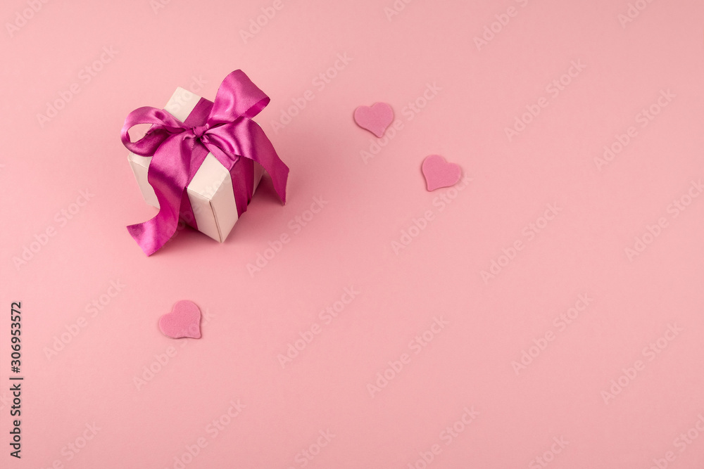 top view gift box with festive satin ribbon bow and three hearts on a soft pink background with copy space