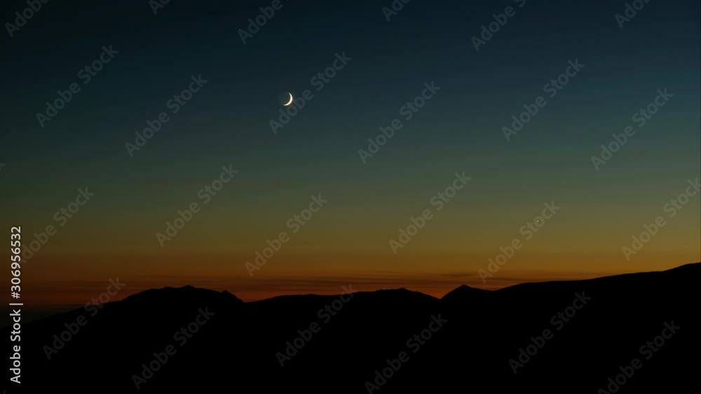 Night to day timelapse of crescent moon rising over the mountains at dawn. Night to day timelapse of crescent moon rising over the mountains at dawn.
