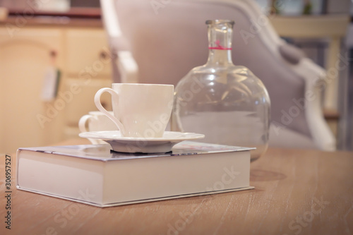 Focus selection: A white coffee cup placed on a book at a table and a glass bottle near it. In a light, comfortable atmosphere