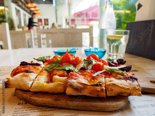 Photography Wide closeup of a Margherita pizza topped with basil, cherry tomatoes, and Burrata cheese, served at an authentic Italian restaurant