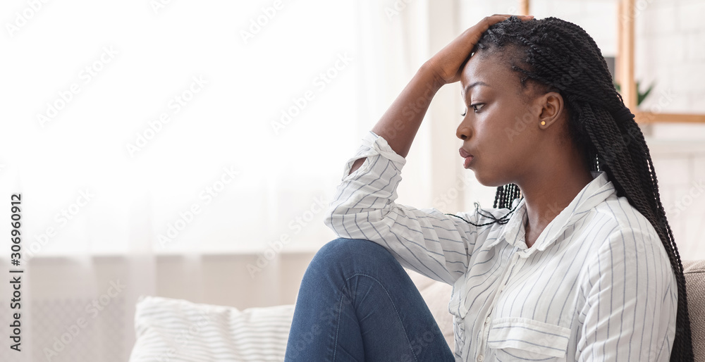 Thoughtful black girl sitting on couch at home, feeling lonely Thoughtful black girl sitting on couch at home, feeling lonely