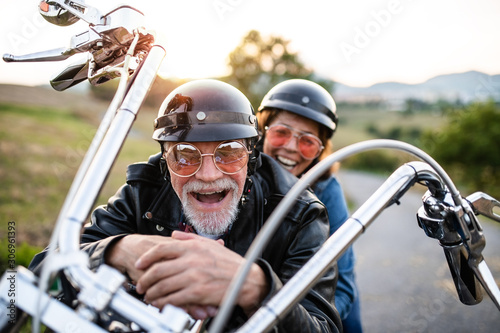 A cheerful senior couple travellers with motorbike in countryside. photo