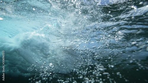 Underwater footage of a breaking wave with a surfboard seen from the water.