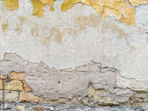 Old looking facade wall with pieces of old yellow facade left of a color that used to be with rough texture of bricks showing and ready to be renovated