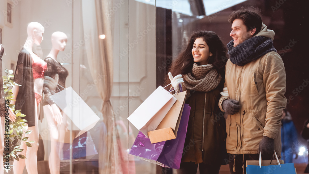Couple Standing Outdoor Of Clothing Store Pointing Finger At Shopwindow Couple Standing Outdoor Of Clothing Store Pointing Finger At Shopwindow