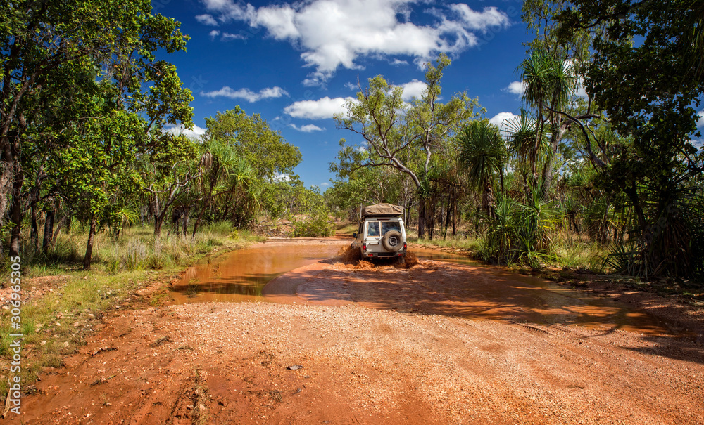 Western Australia – Flooded Outback gravel road with 4WD car crossing the waterhole at the savanna